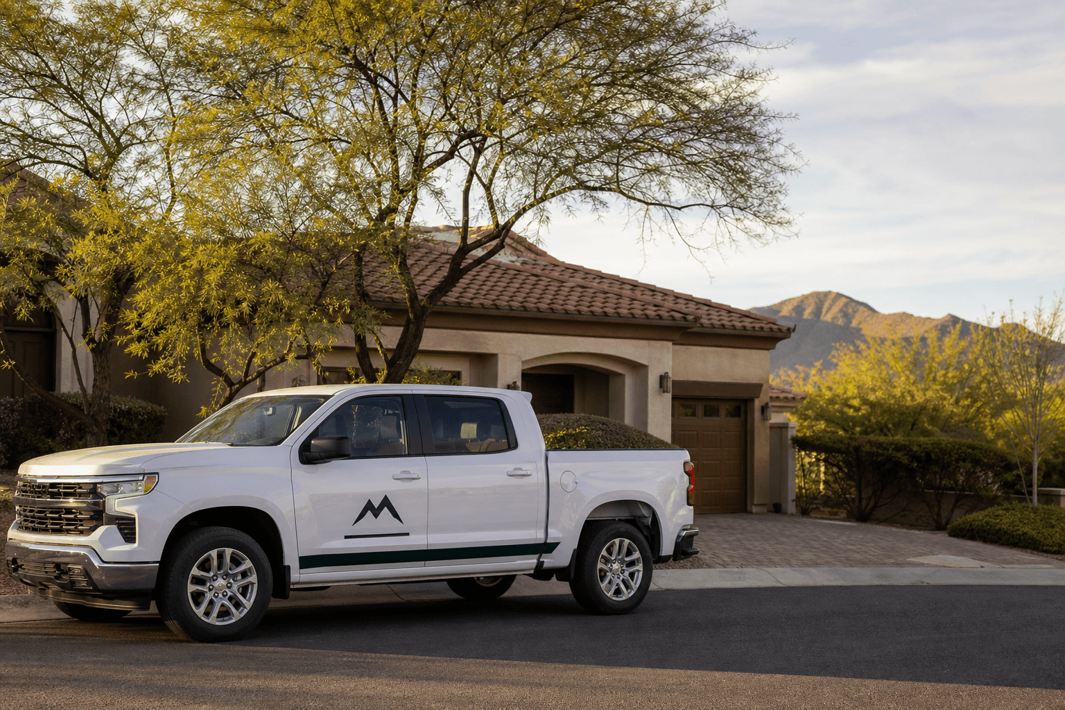 An Anthem Summit Roofers work truck parked on a quiet Anthem cul-de-sac in front of a Spanish Colonial home, with the eastern Daisy Mountain ridge faintly in the distance.