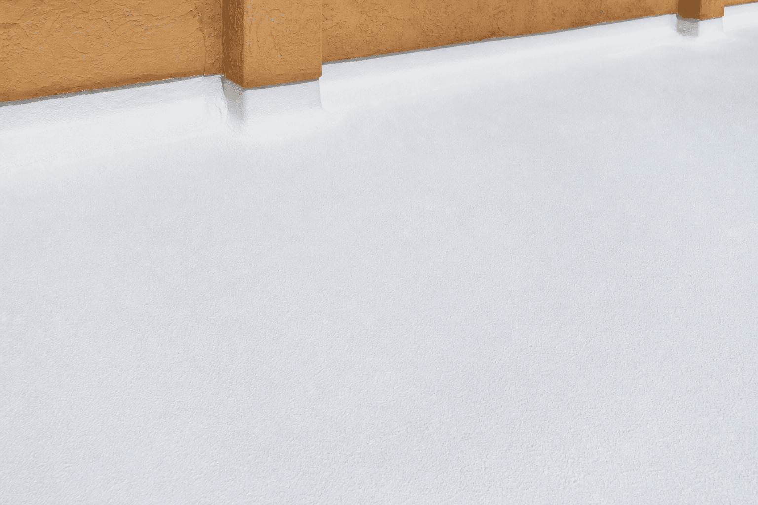 Close-up of a freshly recoated foam roof — sprayed polyurethane foam under a clean white elastomeric topcoat with subtle granule texture, parapet wall in warm Tuscan stucco at the top of the frame.